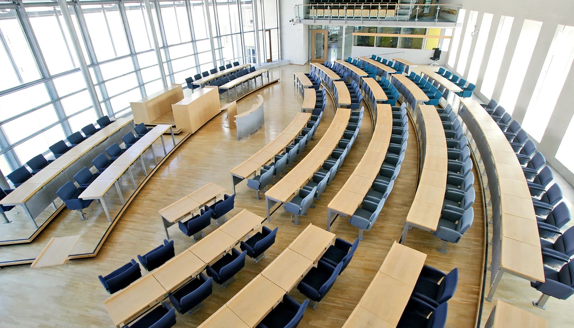 Leerer Plenarsaal mit geordneten Sitzblöcken und zentralem Mittelgang.