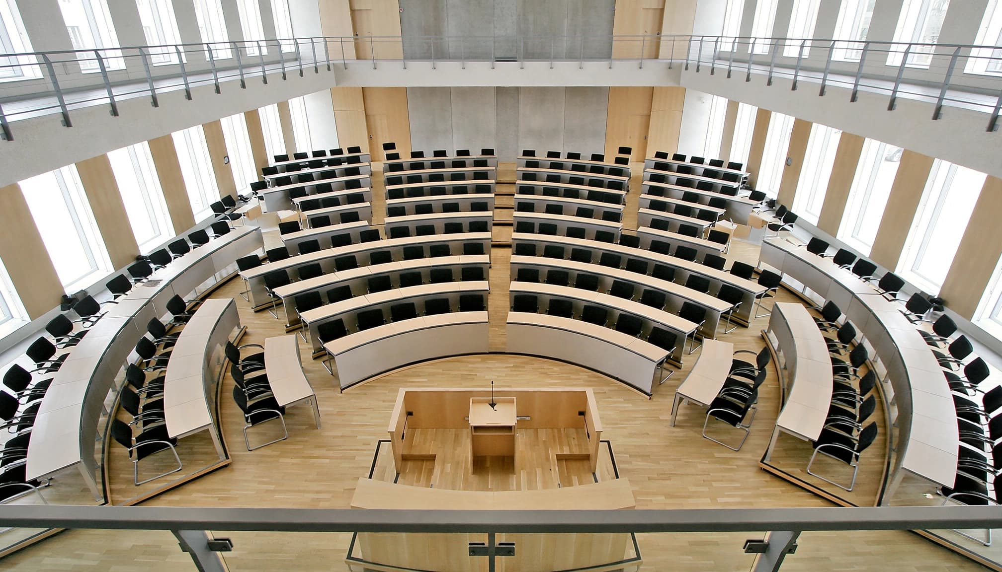 Leerer Plenarsaal mit Sitzblöcken und Rednerpult.